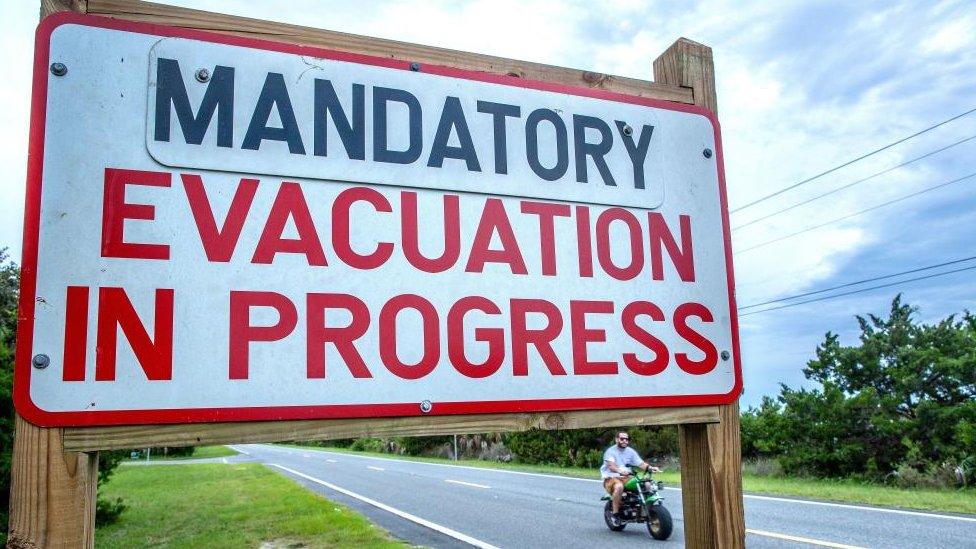 A person rides a bike near a 'mandatory evacuation' sign, as the town prepares for Hurricane Idalia, in Cedar Key, Florida,