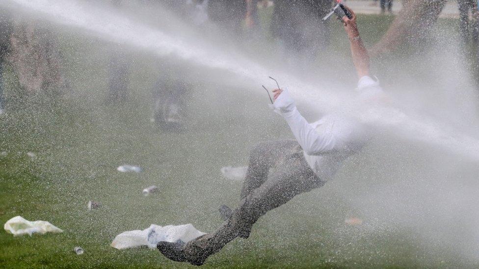 A man is doused by a water cannon during clashes as people gather at the Bois de la Cambre/Ter Kamerenbos park in Brussels