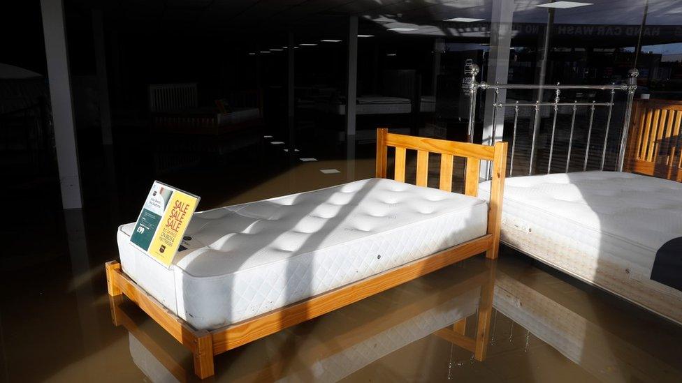 A bed in the window of a shop stands in floodwater