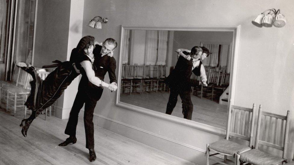 Legendary ballroom dancer Vernon Castle (1887 - 1918) lifts his wife and partner Irene (1893 - 1969) as they dance before a large mirror in a dance studio, New York, 1914