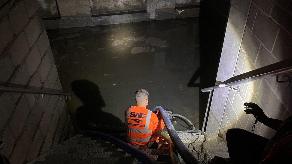 A contractor pumps water from the basement in a building at Hallsville Quarter