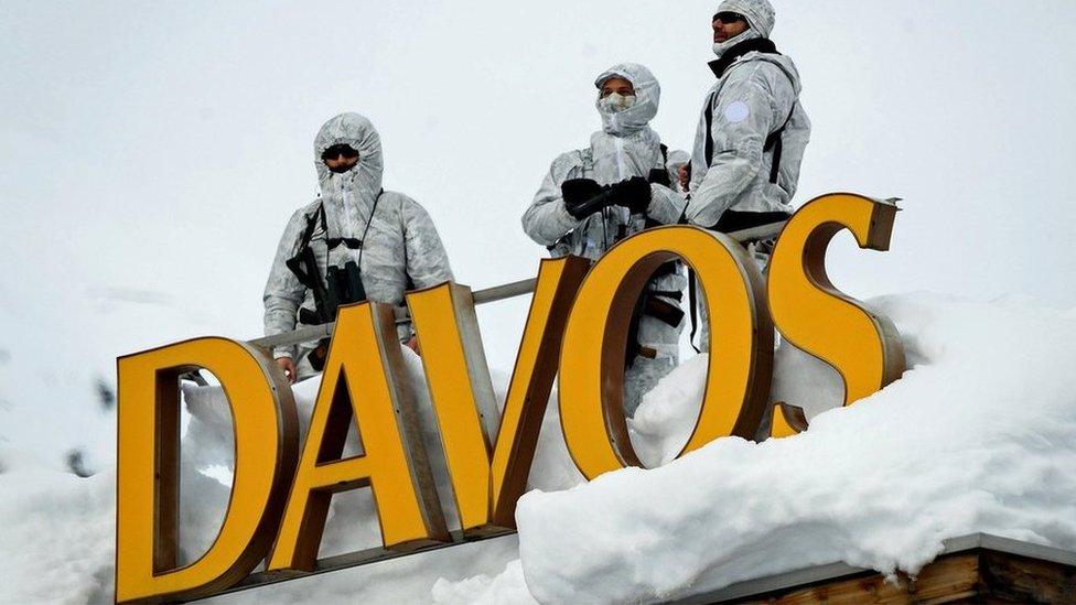 Armed security personnel stand guard on the rooftop of a hotel, next to letters reading "Davos"