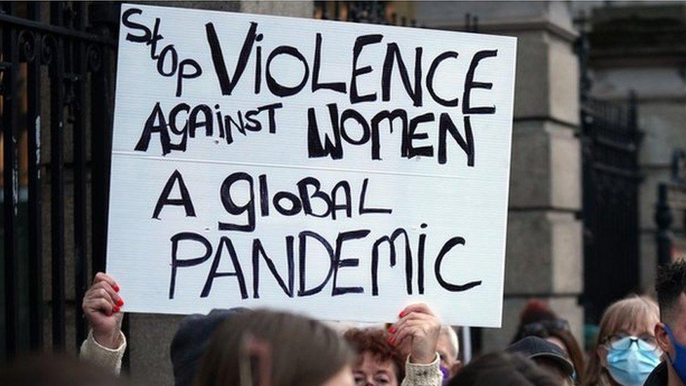 A protestor holding a sign that reads: Stop violence against woman - a global pandemic