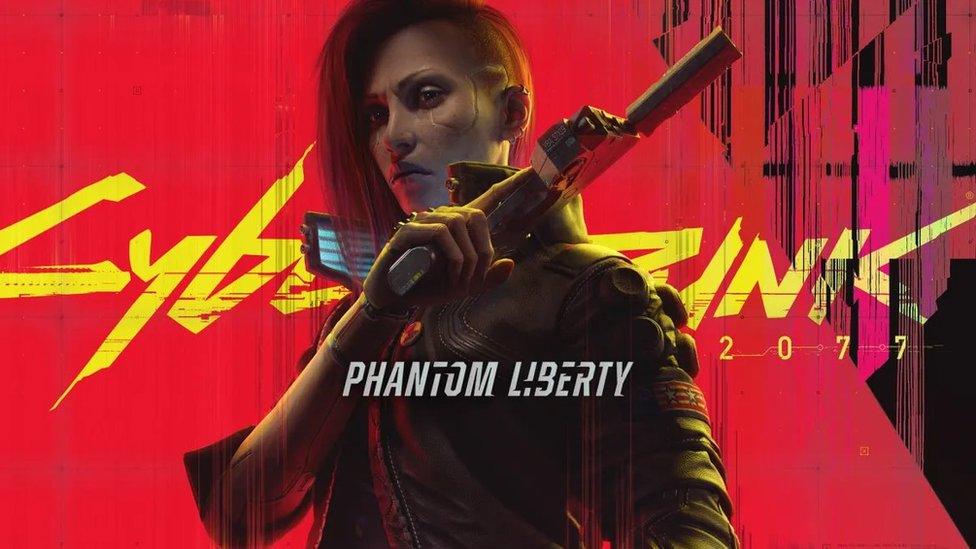 A character from Cyberpunk 2077 stands against a red background with the game's title written in yellow font. The subtitle Phantom Liberty is written across the character's body in white. The female character looks mean, and has a scar around her eye. She's dressed in futuristic leather jacket and holds a silenced pistol.