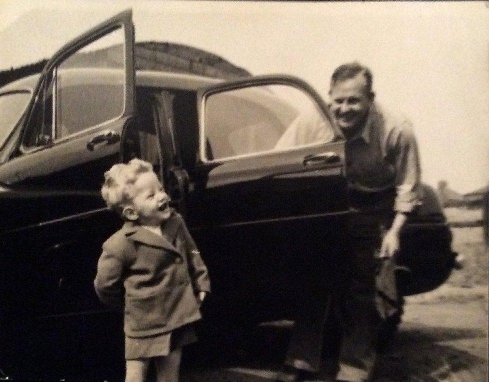 Ian as a child laughing with his dad by a car