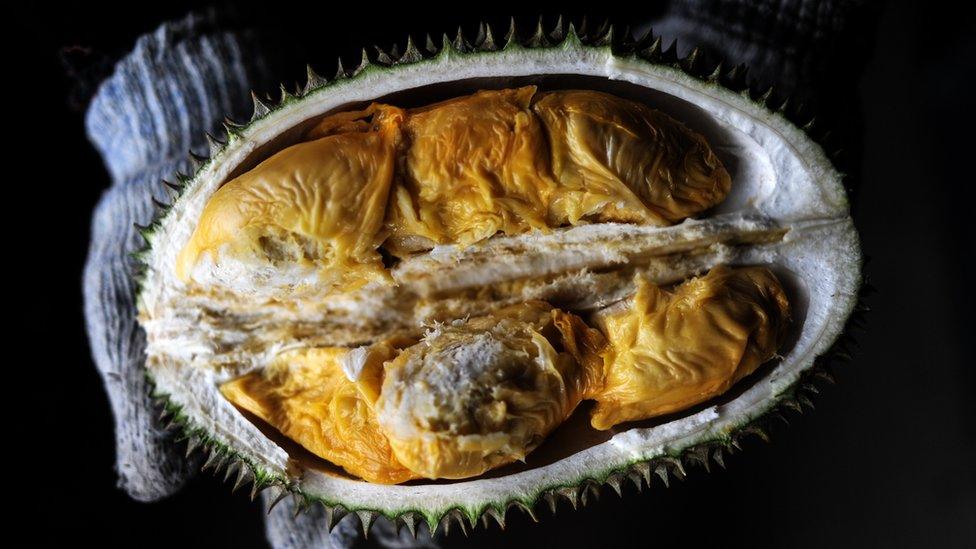 A vendor displays the cross section of a durian at a roadside fruit shop