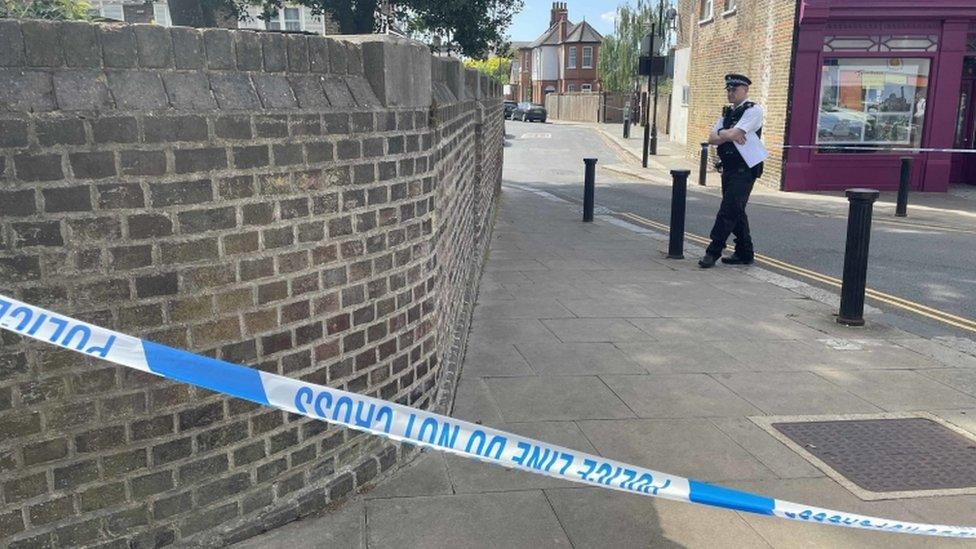 A police officer stands near the alleyway off Church Gardens, South Ealing