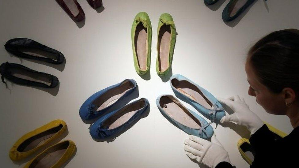 An employee poses as she adjusts a display of ballet pumps belonging to Audrey Hepburn