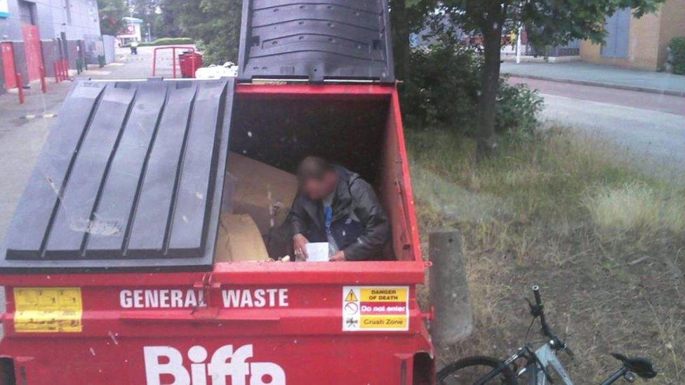 Homeless man sitting inside Biffa recycling bin