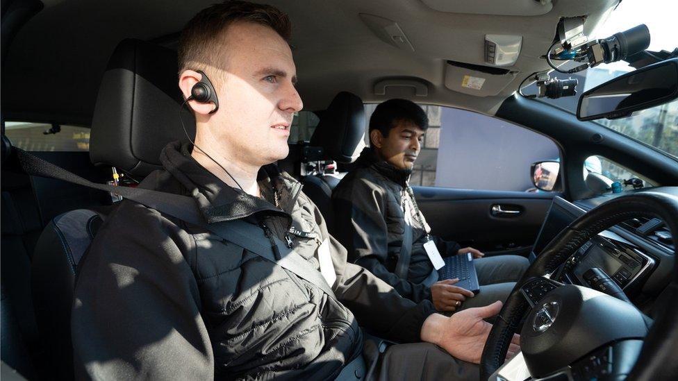 Two people sit inside a self-driving Nissan Leaf car