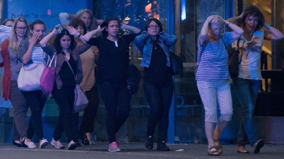 People leaving shopping centre with hands on their heads