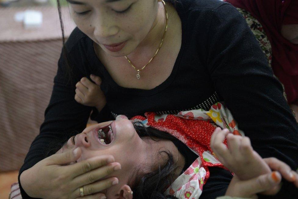 This picture taken on February 10, 2013 shows Indonesian mother Desi (top) trying to calm her four and half year-old daughter Kania as doctors (back R) perform her circumcision in Bandung