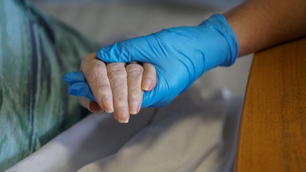 Hand wearing vinyl glove holds elderly woman's hand