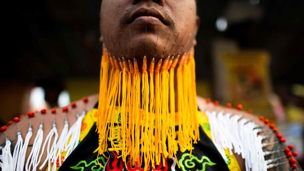 A devotee of the Loem Hu Thai Su shrine waits to parade with needles pierced through his chin