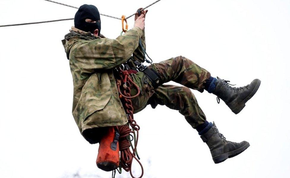 An activist hangs from a rope between trees at a makeshift camp