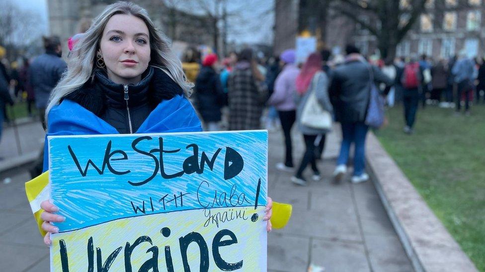 Kristina, a Ukrainian student, holding a sign saying 'we stand with Ukraine'