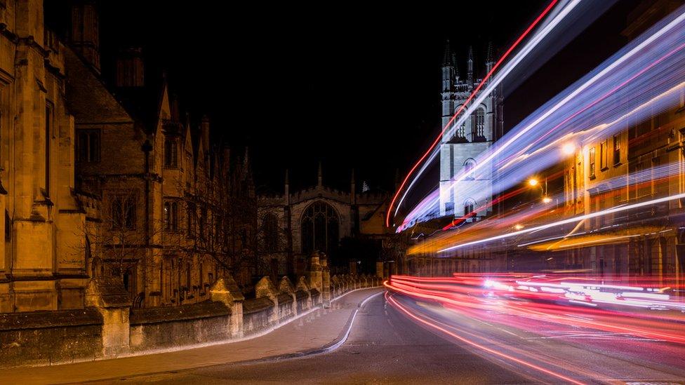 Traffic light trails past Oxford University college buildings on High Street