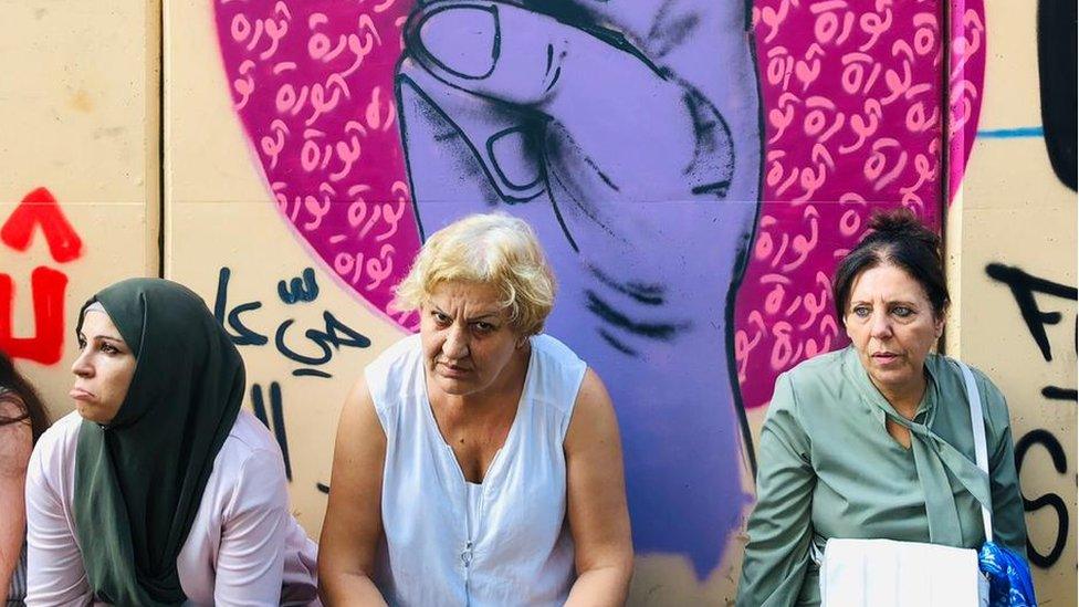 Women sit in front of protest graffiti in Beirut