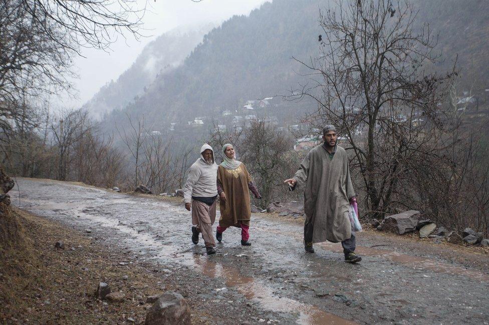 A Kashmiri family walks towards a vehicle as they leave home