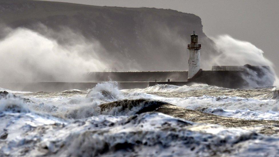 Stormy seas with sea water breaking over a sea wall near a lighthouse