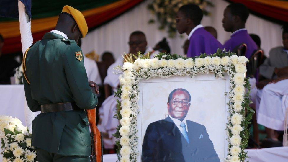 A soldier stands beside a picture of former Zimbabwean President Robert Mugabe during a church service at his rural village in Kutama, Zimbabwe, September 28, 2019