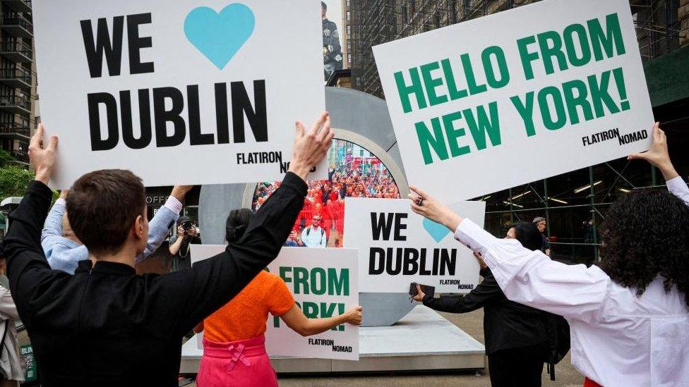 People hold signs as they greet during the reveal of The Portal, a public technology sculpture that links with direct connection between Dublin, Ireland and the Flatiron district in Manhattan, in New York City, U.S., May 8, 2024.