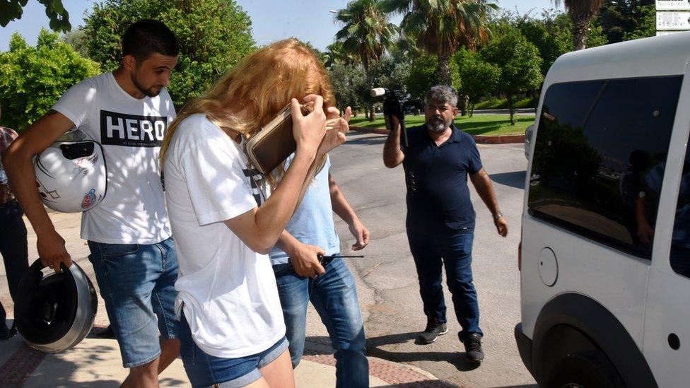 A couple wearing a white T-shirt with the word "hero" on it being escorted to a police vehicle