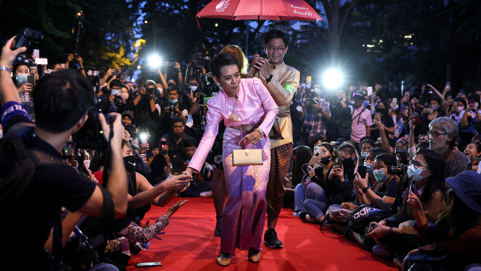 Jatuporn 'New' Saeoueng wears a pink silk dress and shakes hands with other activists on a red carpet at a satirical fashion show protest in Bangkok in 2020