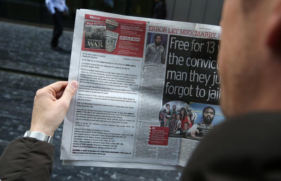 a man holds a newspaper with an advert informing victims how to claim for compensation if they were sexually abused by broadcaster Jimmy Savile on April 22, 2014 in London, England