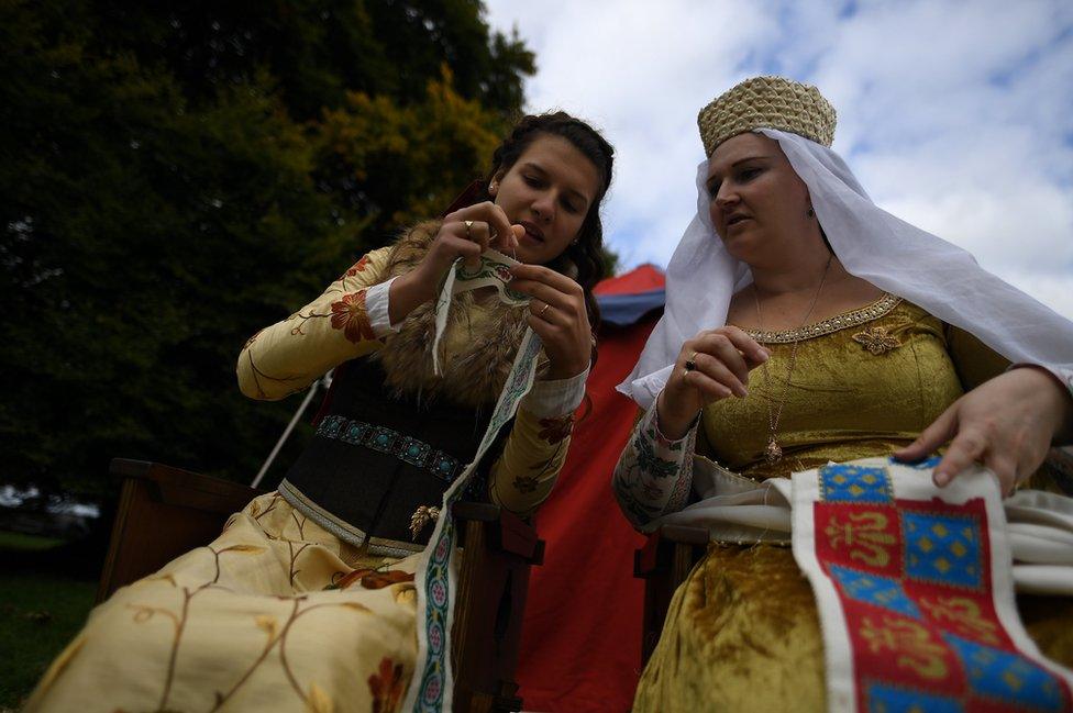 Two women dressed in medieval costume sew together