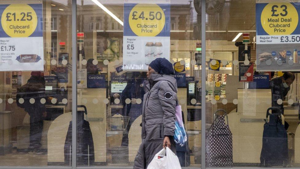 A woman carrying a shopping bag walks past a Tesco supermarket