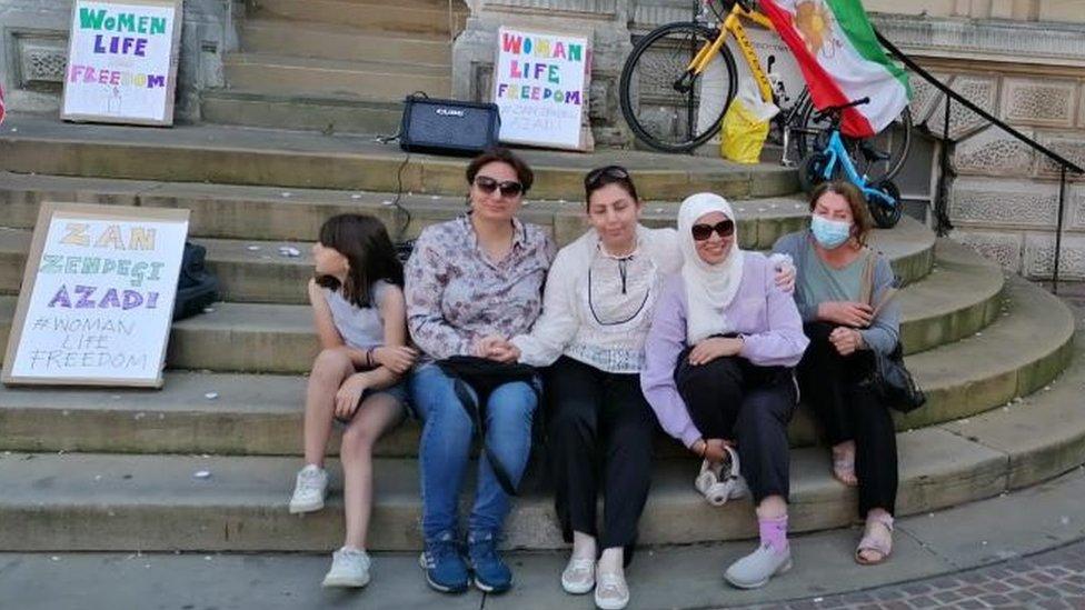 Four women and a girl sit on the steps of Ipswich Town Hall during a vigil.