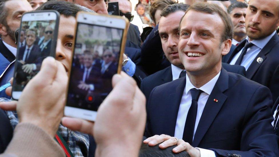 French President Emmanuel Macron is surrounded by security as he greets children in the streets of Algiers on December 6, 2017.