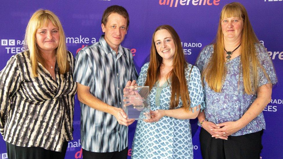 Three women and a man hold a glass award