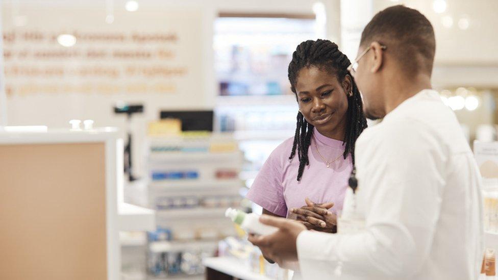 Young woman listening to advice of male pharmacist at pharmaceutical industry - stock photo