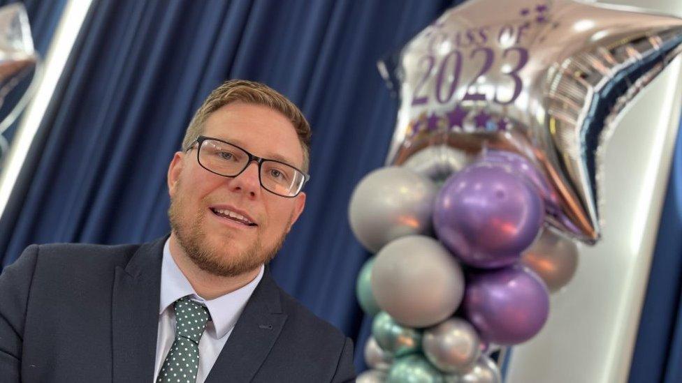 teacher Olly Denton in front of a star balloon that reads 'Class of 2023'