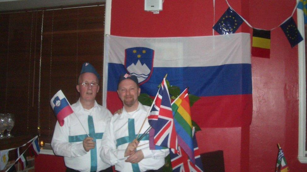 Two men holding European flags in front of a flag backdrop