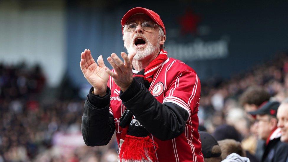 A Bristol City fan wearing a red shirt and hat cheers his team on against Leicester City at Ashton Gate