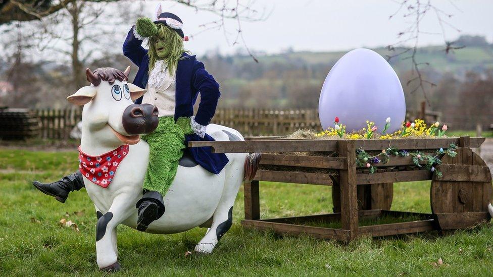 A person in a Grinch costume sitting on a large fake cow