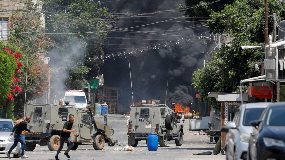 Palestinians run for cover as Israeli military vehicles move through Jenin, in the occupied West Bank (3 July 2023)