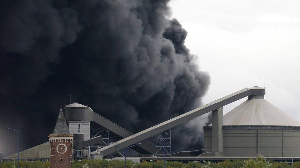 Large cloud of thick black smoke billows from the factory building.