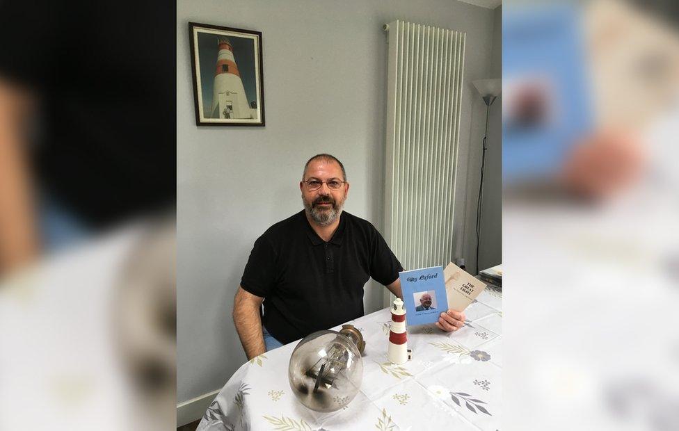 Adrian Underwood with his father's books and a model lighthouse he has at his home in Ireland