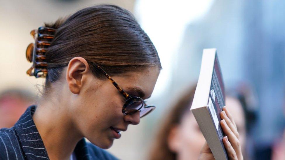 Kaia Gerber hides her face behind a book in front of photographers, outside Valentino, during Paris Fashion Week Haute Couture Fall/Winter 2019/20, on July 03, 2019 in Paris, France