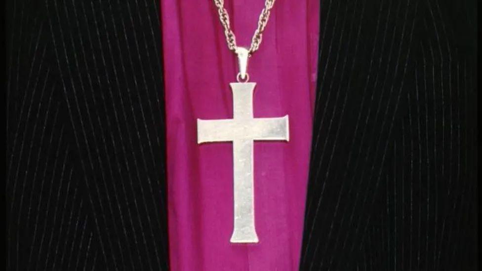 A silver necklace of a cross on religious purple and black robes.