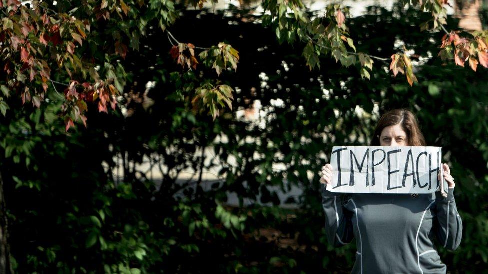 A woman holds up an Impeach sign to the presidential motorcade