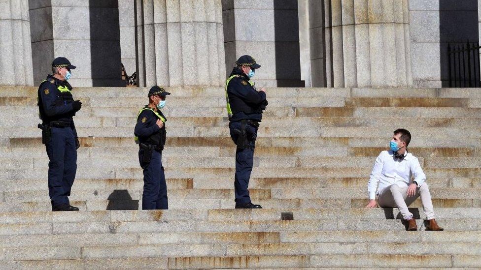 Three police officers wearing masks in Melbourne speak to a civilian