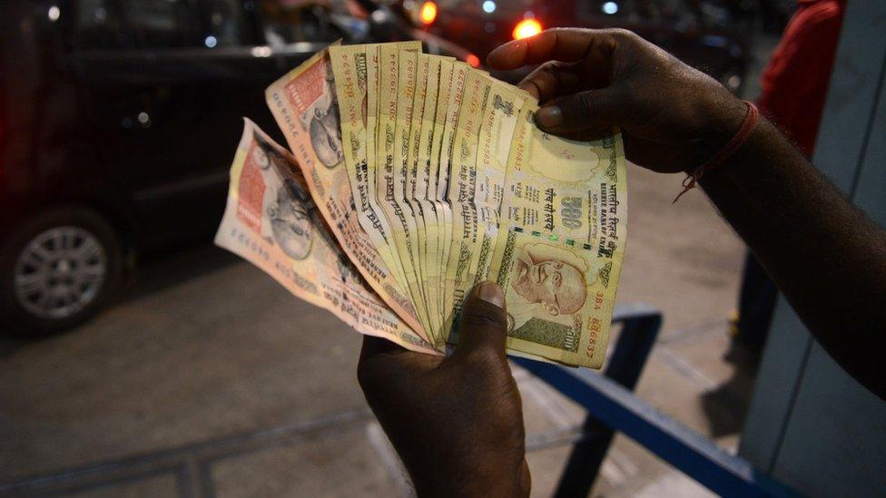 An Indian fuel station employee checks a 500 and 1000 rupee notes as residents queue up at a fuel station in Siliguri on November 8, 2016.