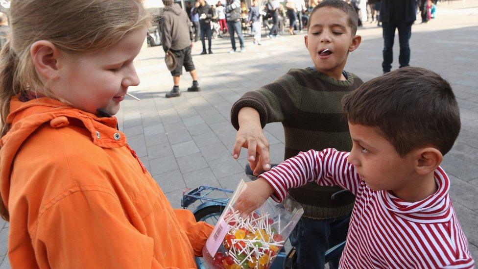 Lea, 12 (L), gives lollipops to Syrian refugee children at a welcome festival (Willkommensfest) for migrants on September 19, 2015 in the Karolinenviertel neighborhood of Hamburg, Germany