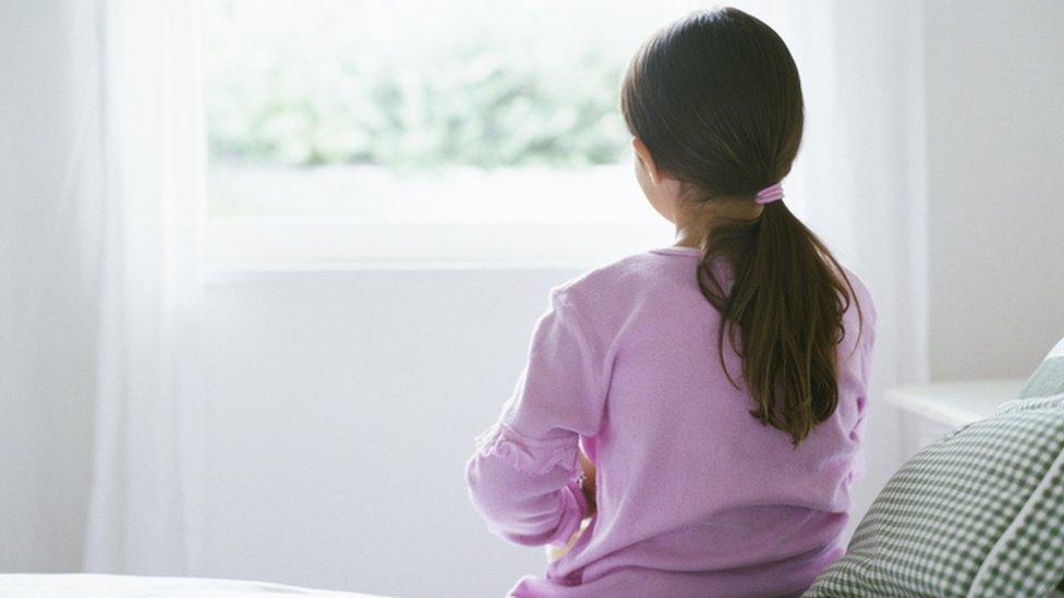 A young girl sat on a bed facing away from the camera