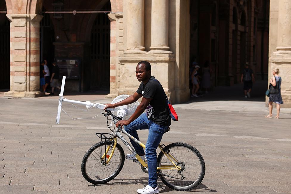 A man carries an electric fan with a bike in Bologna, Italy